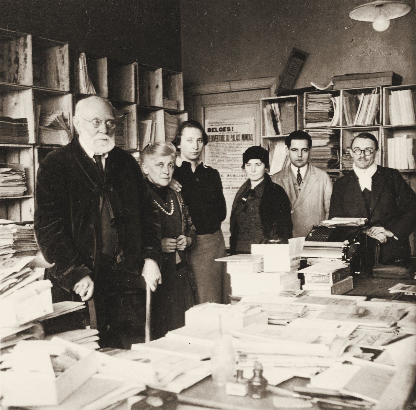 Paul Otlet, white-bearded, stands with five colleagues among stacks of papers and card files in his office.